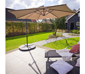 Grote taupe Nexxt Zweefparasol met Beschermhoes in tuinopstelling met veel schaduw en comfortabele zithoek.

