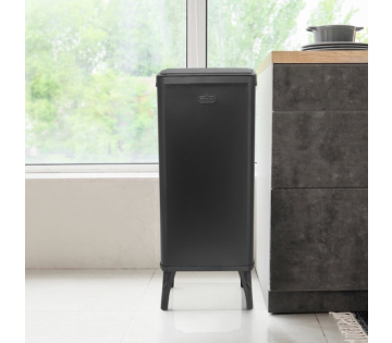Zwarte prullenbak met sensor naast het keukenblok, strak vormgegeven en ruimtebesparend geplaatst bij het raam.
