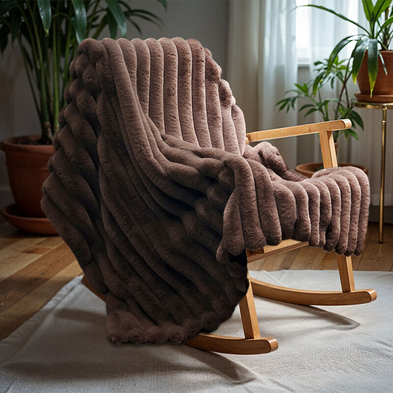 Zachte Pom Rabbit Fur plaid in Taupe op een schommelstoel voor een knusse en stijlvolle zithoek.