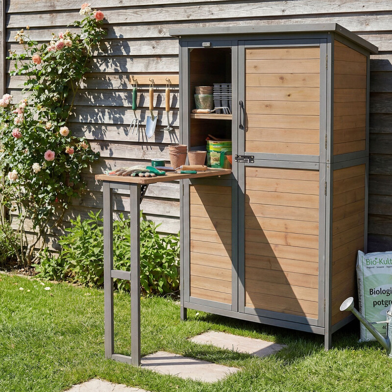 Tuinhuis met uitgeklapte werkbank in houtkleur en grijs frame naast een schutting, ideaal voor tuinwerk en verpotten.