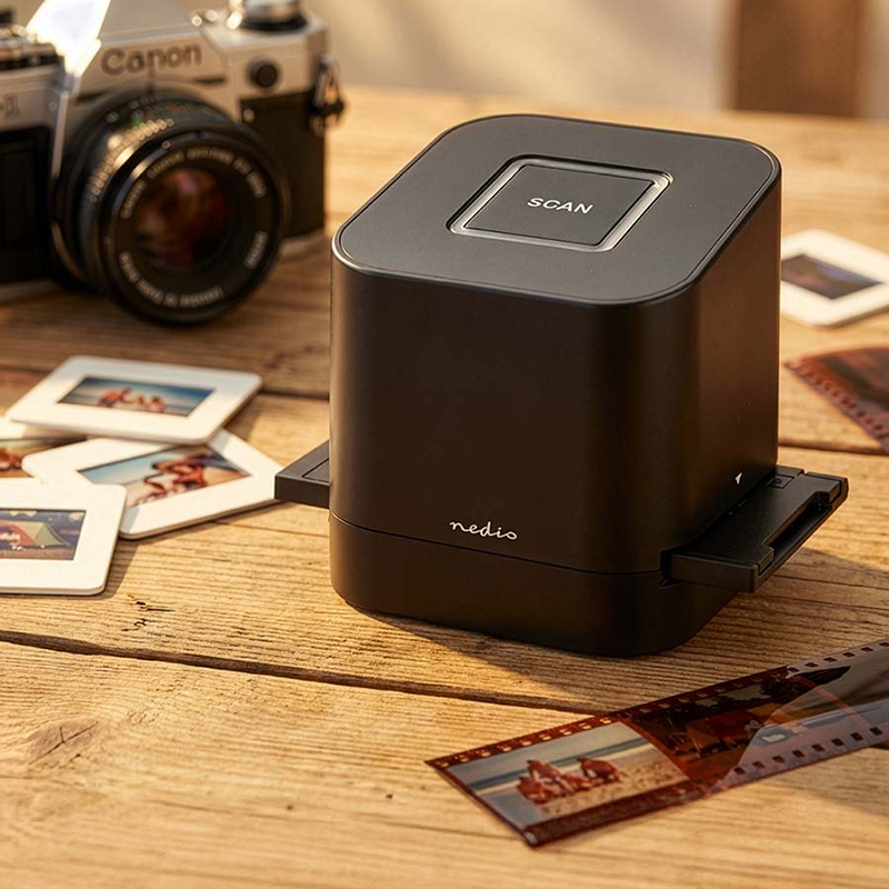Compacte Nedis filmscanner op houten tafel met dia’s en camera op de achtergrond