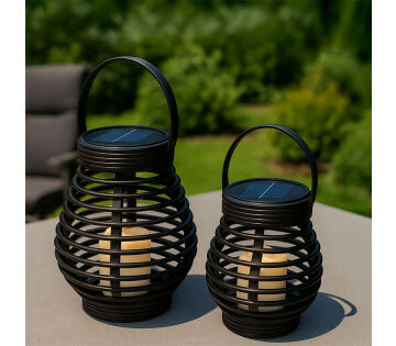 Twee FlinQ Solar Lantaarns Bottassano in rotan stijl met warm LED-licht, geplaatst op een tafel in de tuin.