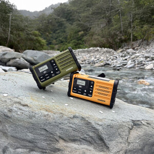 Sangean SDR-800DAB noodradio groen en geel in natuur bij rivier, robuuste noodradio voor outdoor gebruik.