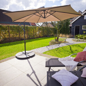 Grote taupe Nexxt Zweefparasol met Beschermhoes in tuinopstelling met veel schaduw en comfortabele zithoek.

