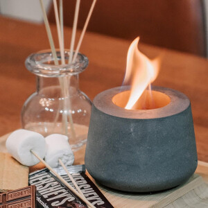 Grijze bio-ethanol tafelhaard naast geurstokjes en marshmallows voor een sfeervol interieurmoment.